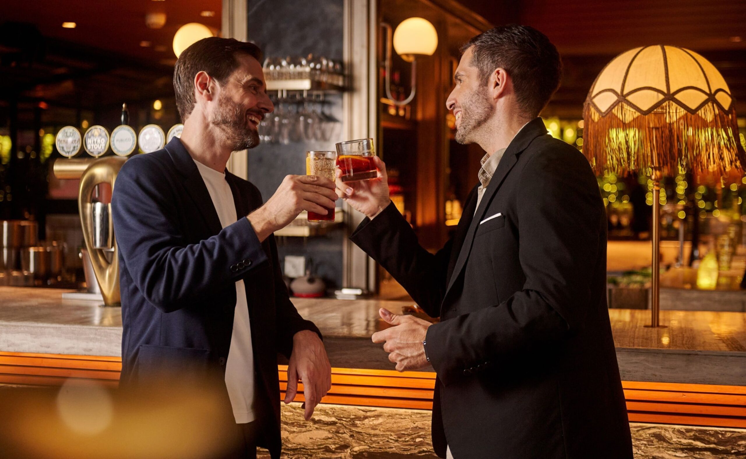 Two guests raising glasses over drinks at the bar at Publico Ristorante, Robertson Quay